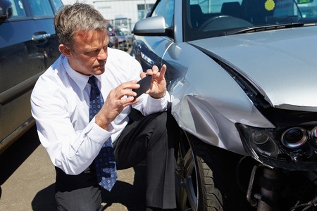 A man using his phone to take a photo of the damage to his car.