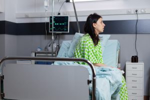A woman is sitting on a hospital bed looking into the distance.