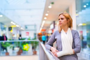 A woman with a bandaged arm in a brace stands in a shopping centre